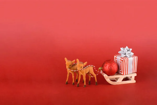 Boże Narodzenie lub Nowy Rok projektowania tła. Renifer z saniami zimowymi i pudełkiem prezentów na czerwonym tle. Tło świąteczne z miejscem na tekst. — Zdjęcie stockowe