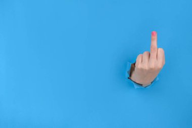 Mavi yırtık kağıtta küçük bir el, orta parmağı gösteriyor, saldırgan bir hareket. Siktir git, konsept. Feminizm kavramı. Kadın üstünlüğü onaylamıyor.