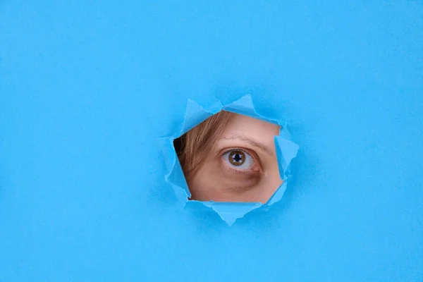 Part of woman\'s face eye with an enema trauma of a woman looking into camera, victim of domestic violence. Behind broken wall or torn paper, on blue background. Space for text, feminist design