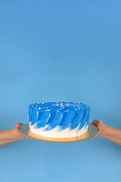 Girl's hands are holding beautiful and tasty cake with white and true blue color cream on a blue background with place for text. — Stock Photo, Image