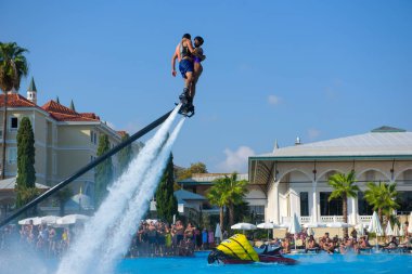 ANTALYA TURKEY 27 SEPT 2019: uçuş panosunda genç bir kızla dalış kıyafeti giyen bir adam havuz otelinde uçuyor ya da su basıncı kuvveti ile. Güneşli havada kaydediliyor, genel plan.