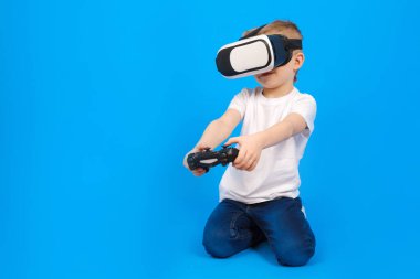 VR gözlük takan çocuk sanal dünyayla etkileşimde, beyaz polo ve mavi arka planda kot pantolon giyiyor. Yenilikçi teknoloji ve eğitim ve eğlence kavramı.