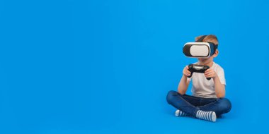 VR gözlük takan çocuk sanal dünyayla etkileşimde, beyaz polo ve mavi arka planda kot pantolon giyiyor. Yenilikçi teknoloji ve eğitim ve eğlence kavramı.