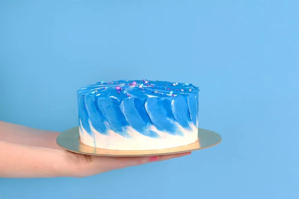 Girl's hands are holding beautiful and tasty cake with white and true blue color cream on a blue background with place for text. — Stock Photo, Image