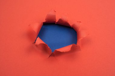 Kırmızı kağıtta yırtık kenarları ve mavi arka planı olan yırtık yuvarlak bir delik. İleti için boşluk, kağıt dokusu.