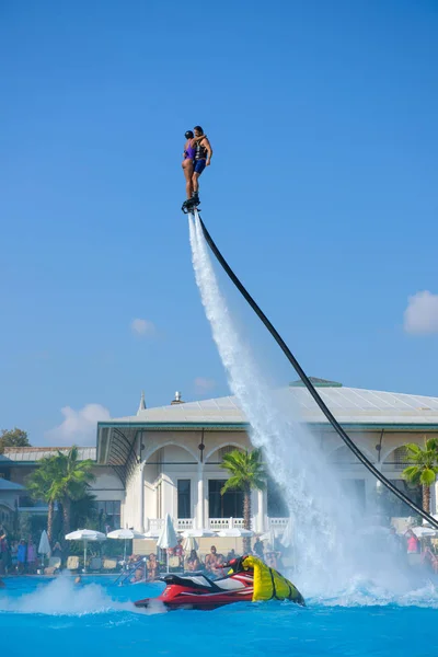 ANTALYA TURKEY 27 SEPT 2019: Homem de fato de mergulho com jovem no mosca de prancha em hotel de piscina em jato de ar ou força de pressão de água. gravação em tempo ensolarado, plano geral. — Fotografia de Stock