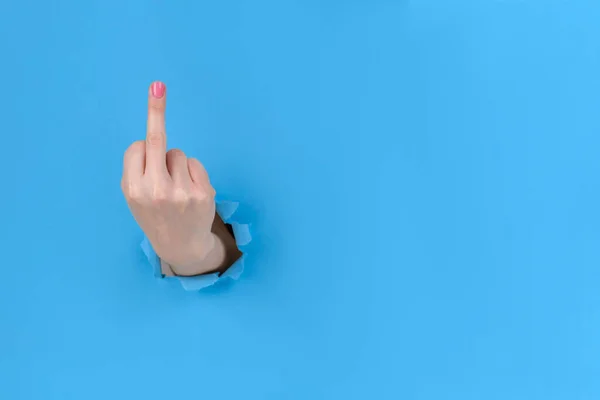 Girl hand on blue torn paper background, shows middle finger, an offensive gesture. FUCK you, concept. The concept of feminism female superiority disapproval — ストック写真