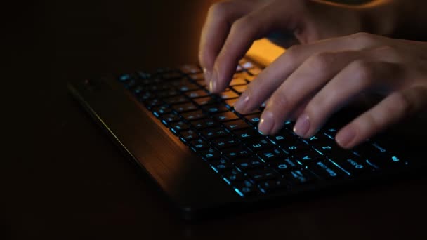 Close-up vrouwen hand type tekst op LED gloeiende toetsenbord in de voorkant van de computer op kantoor. Meisje werkt op de computer achter het LED-toetsenbord. Zakenvrouw werkt op tablet computer. — Stockvideo