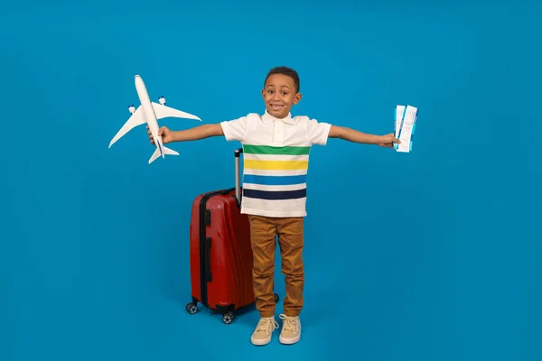 Viajero turista chico afroamericano sobre fondo azul. Pasajero viajando al extranjero durante el fin de semana. Vuelos al viaje a pie fuera de la maleta para guardar pasaporte, tarjeta de embarque, billetes de avión — Foto de Stock