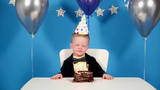 Szczęśliwy chłopczyk na przyjęciu urodzinowym zamyka oczy wypowiada życzenie i zdmuchuje świeczki na torcie czekoladowym na świątecznym tle z balonami i dekoracjami z gwiazd. Plan ogólny urodziny — Wideo stockowe