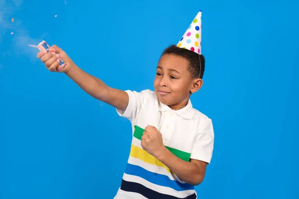 Afrikai amerikai fiú felrobban csapkodó tartja a kezét öltözött fehér póló és party sapka áll a kék stúdió háttérben. Születésnapi koncepció és ünnepek party koncepció helyet a szöveges. — Stock Fotó