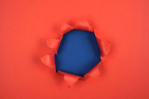 引き裂かれた縁と青の背景を持つ赤い紙に丸い穴をあける。メッセージ、紙の質感のためのスペース. — ストック写真