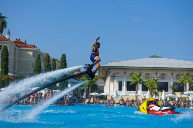 ANTALYA TURKEY 27 SEPT 2019: uçan giysili adam havuz otelinde havuz jeti veya su basıncı kuvvetiyle uçuyor. Güneşli havada kaydediliyor, genel plan.