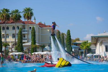 ANTALYA TURKEY 27 SEPT 2019: uçuş panosunda genç bir kızla dalış kıyafeti giyen bir adam havuz otelinde uçuyor ya da su basıncı kuvveti ile. Güneşli havada kaydediliyor, genel plan.