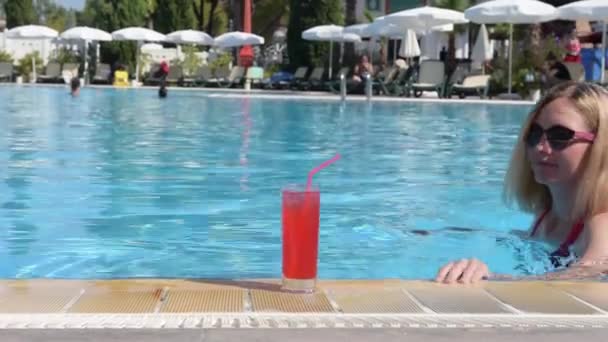 Girl drinks a cocktail of Sex on beach in the pool. Beautiful girl in sun  protective glasses and red swimsuit swims in the pool and drinks red  alcoholic cocktail Sex on the