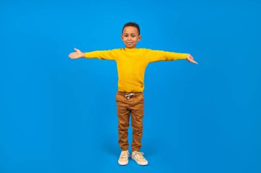 Mutlu Afro-Amerikalı çocuk zafere ve başarıya seviniyor ve gülümsüyor, ellerini kaldırıyor, mavi stüdyonun homojen arka planında. Kazanma konsepti, kazanma gayesine ulaşmak..