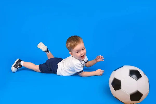 Niño portero está acostado jugando fútbol o de pie en el gol se perdió la pelota en el gol en un fondo de estudio azul. — Foto de Stock
