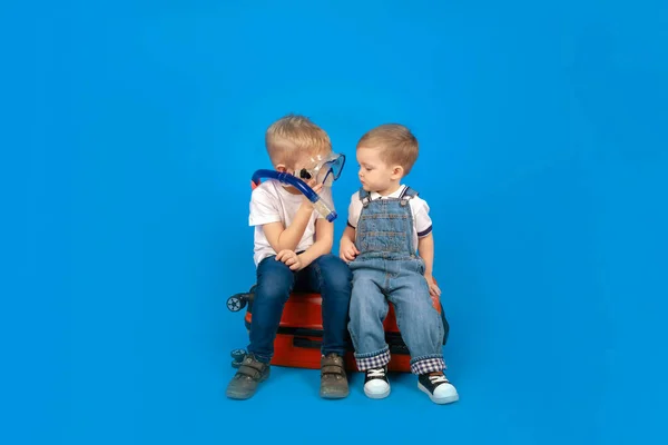 Two happy baby tourists sitting on a red suitcase look at each other smiling and crooked. Funny kids travel. Tourism concept — Stock Photo, Image