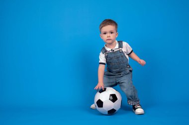 Küçük futbol şampiyonu. Futbol topuyla yerde oturan sevimli Avrupalı bebek stüdyoda mavi arka planda fotokopi alanı, spor konsepti