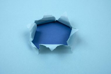 Yırtık kenarları ve mavi arka planı olan mavi kağıtta yırtılmış yuvarlak bir delik. İleti için boşluk, kağıt dokusu.