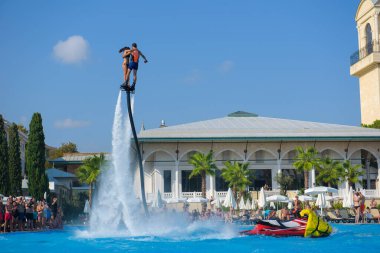 ANTALYA TURKEY 27 SEPT 2019: uçuş panosunda genç bir kızla dalış kıyafeti giyen bir adam havuz otelinde uçuyor ya da su basıncı kuvveti ile. Güneşli havada kaydediliyor, genel plan.