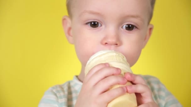 Μικρό χαριτωμένο ξανθό αγόρι τρώει ενώ απολαμβάνουν κρύο παγωτό στο Κύπελλο βάφλα, σε κίτρινο φόντο στούντιο. Κοντινό πορτραίτο προσώπου. — Αρχείο Βίντεο
