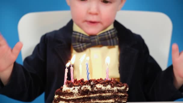 Feliz niño en su cumpleaños cierra los ojos pide un deseo y sopla las velas en un pastel de chocolate sobre fondo azul. Plan maestro de cumpleaños, vacaciones, cumpleaños y concepto de fiesta. de cerca — Vídeos de Stock