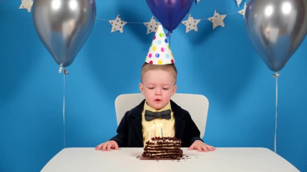 Compleanno del bambino, festa di compleanno che desiderano desiderio e soffiare candele sulla torta, per molto tempo non può spegnere una candela, quasi bruciato il dito sul fuoco su sfondo festivo blu. — Video Stock