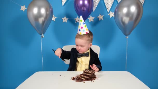 Boy come un pastel de chocolate en una mesa de cumpleaños concepto de fiesta y cumpleaños. — Vídeos de Stock
