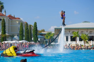 ANTALYA TURKEY 27 SEPT 2019: uçuş panosunda genç bir kızla dalış kıyafeti giyen bir adam havuz otelinde uçuyor ya da su basıncı kuvveti ile. Güneşli havada kaydediliyor, genel plan.