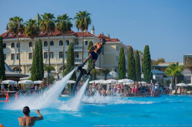 ANTALYA TURKEY 27 SEPT 2019: uçan giysili adam havuz otelinde havuz jeti veya su basıncı kuvvetiyle uçuyor. Güneşli havada kaydediliyor, genel plan.