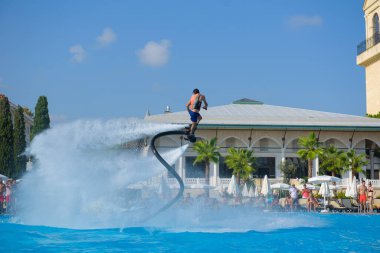 ANTALYA TURKEY 27 SEPT 2019: uçan giysili adam havuz otelinde havuz jeti veya su basıncı kuvvetiyle uçuyor. Güneşli havada kaydediliyor, genel plan