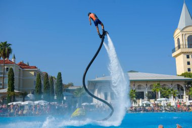ANTALYA TURKEY 27 SEPT 2019: uçan giysili adam havuz otelinde havuz jeti veya su basıncı kuvvetiyle uçuyor. Güneşli havada kaydediliyor, genel plan