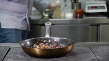 Lokanta mutfağında erkek aşçı sıcak fırında kızarmış mantar, et ve soğan hazırlıyor. Ayçiçeği yağı ekler ve ahşap spatula kışkırtıcısıyla karıştırır