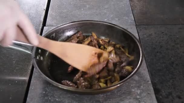 Kook roostert hertenvlees met uien en champignons op hete pan in restaurant keuken. Chef roert en gooit ingrediënten in pan. — Stockvideo