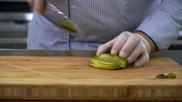 Chef i gummihandskar skär inlagd gurka med kniv på trä bambu skärbräda. — Stockvideo