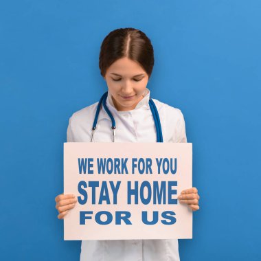 Beyaz önlüklü doktor kadın, koronavirüs salgını sırasında evde kalması ve kendini izole etmesi için pankart tutuyor. Sağlık görevlileri 