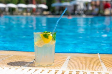 Rahatlatıcı bir tatil konsepti için dinlendirici Mojito kokteyli ve dinlenme sandalyeleri. Açık havuz arka planı.