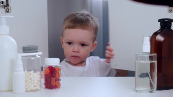 Criança loira pequena abre kit de primeiros socorros, abre frasco de vitaminas vermelhas em forma de ursos. Leva uma pílula, come, fecha o armário e deixa. — Vídeo de Stock