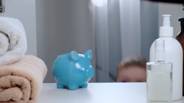 Bělošský blonďák v bílém tričku dává do modré prasečí banky nahromaděné dvě mince, zavírá skříň a odchází. Dítě šetří peníze, sbírá peníze na sladkosti, hračky nebo dárky. Pohled POV zevnitř — Stock video