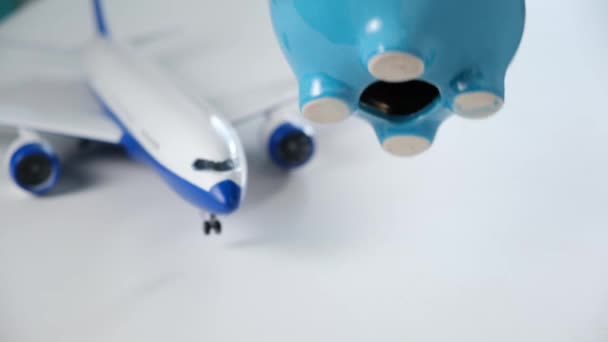 Homem com as mãos sacude moedas de cerâmica azul piggy Bank contra o fundo do modelo plástico de um avião. Dinheiro para passagens aéreas recolhidas ou recolhidas em dinheiro para férias. — Vídeo de Stock