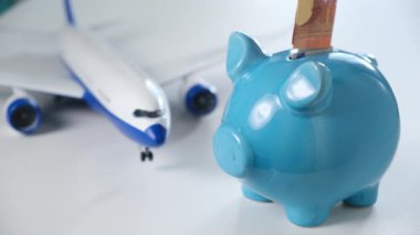 Erkek eli, model uçak oyuncağının arka planına mavi seramik domuz kumbarasına para koyar. Eğlence ve hava yolculuğu için fon çekme kavramı, geleceğe yatırım.