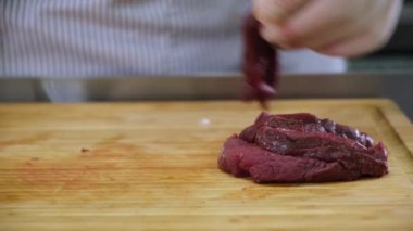Mutfaktaki aşçı, demir bir kaseden büyük bir fileto geyik eti alıyor ve et dilimlerini ahşap bambu tahtasında yemek için kesiyor. Restoranın mutfağında aşçı olarak çalışmak, yemek hazırlamak..