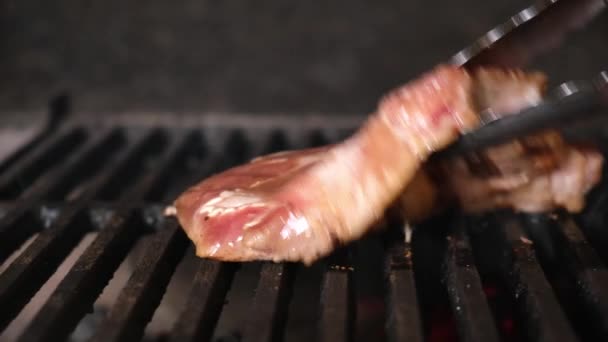 Chefe usando o tong e virar a carne na grelha. Fogo está queimando, cozinhando bife de óleo suculento quente perto. Grill, saboroso bife câmera lenta close-up. Dolly vídeo deslizante. — Vídeo de Stock