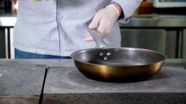 Erkek aşçı, ayçiçeği yağını şişeden restoranların mutfağında sıcak boş kızartma tavasına döker. Yemek pişirmek, mutfakta kızartmak. Dolly eğimli video.