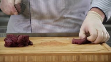 Mutfaktaki aşçı, demir bir kaseden büyük bir fileto geyik eti alıyor ve et dilimlerini ahşap bambu tahtasında yemek için kesiyor. Restoranın mutfağında aşçı olarak çalışmak, yemek hazırlamak..