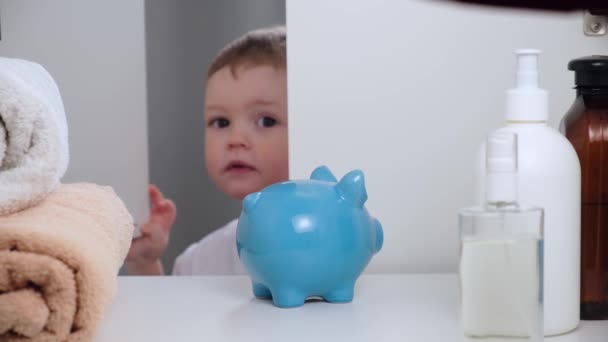 Menino de cabelos justos abre guarda-roupa e leva duas moedas de papel verde do bolso de t-shirt branca, coloca caixa azul Banco neles, não entende como colocar dinheiro em piggy Bank. Vista POV de dentro — Vídeo de Stock