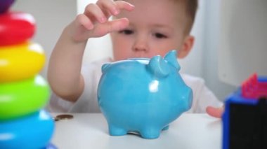 Küçük sarışın beyaz çocuk, çocuk odasındaki dolaptaki gardıroptan mavi seramik domuz kumbarasına para ve sikke koyar. Gelecek, oyuncak ya da hediye için para topluyor..