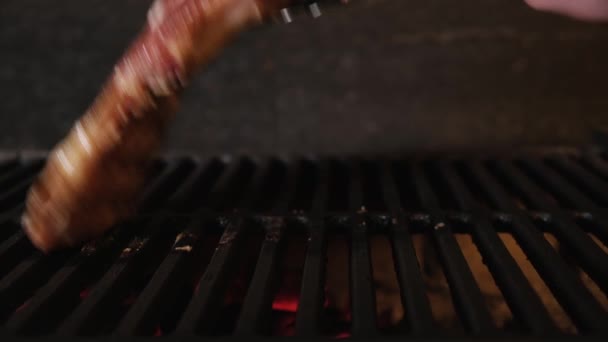 Chef plaatst twee grote rauwe sappige steaks op grill metalen tangen op grill. Het vlees wordt van dichtbij gegrild. Dolly glijdende video — Stockvideo