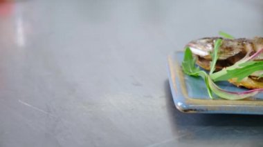 Tüm balık gökkuşağı alabalığı, restoranda, limon ve roka yeşillikleri ile birlikte, tabakta kömür ızgarasında pişiyor. video kamera slaytları